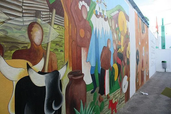 Kolorowy mural z postaciami na białej ścianie uliczki w Asili