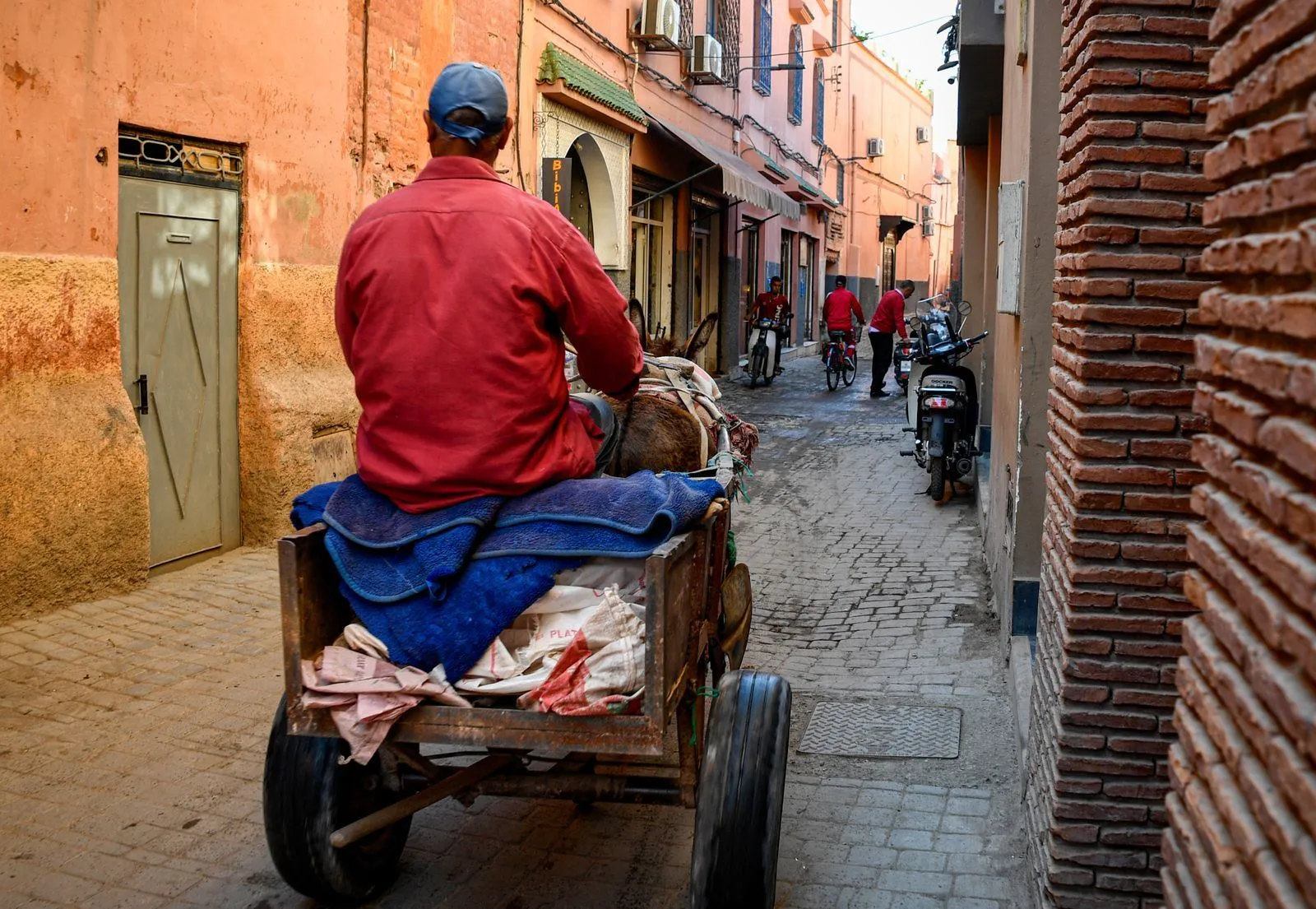 Mężczyzna jedzie wózkiem zaprzężonym w osła wąską uliczką medyny Marrakeszu