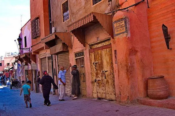 Czerwone ściany domów i przechodnie na ulicy medyny Marrakeszu